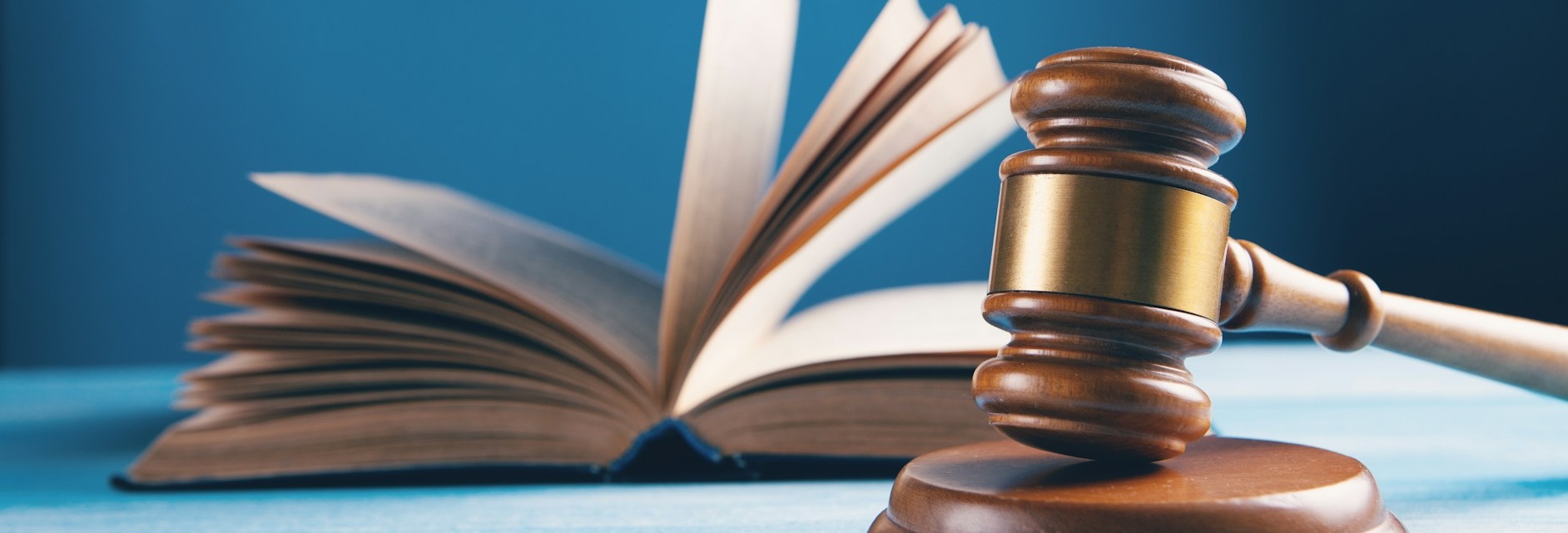 Aufgeschlagenes Buch mit einem Richterhammer im rechten Bildbereich